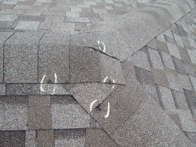 Close-up of four hail-damaged asphalt roof shingles with visible dents marked by chalk