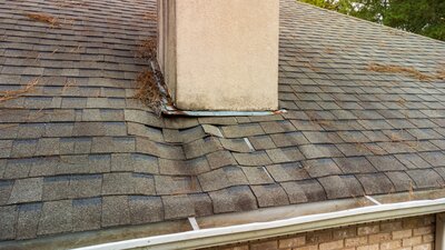 Sagging roofline near a stucco chimney, indicating water damage to the roof decking